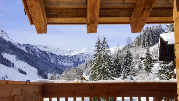 A wooden balcony with a view of snow-covered mountains and trees. - Chalet in Saalbach With Panoramic Sauna (Saalbach-Hinterglemm)