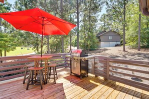 Una terraza de madera con una sombrilla roja, una parrilla y una mesa con dos taburetes.