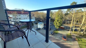 A balcony with a table and chairs, a view of a parking lot, and a building in the background. - Studio in Poland Near Beach Promenade (Swinoujscie)