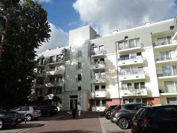 Un edificio residencial de varios pisos con balcones, una zona de estacionamiento y cielo despejado.