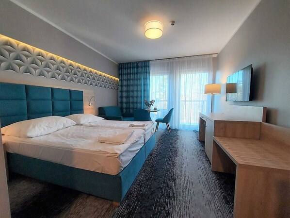 A hotel room with a large bed, a desk, a chair, a TV, and a window with curtains. - Studio in Poland Near Beach Promenade (Swinoujscie)