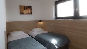 Une chambre avec deux lits, une fenêtre, une lampe fixée au mur et un tableau.