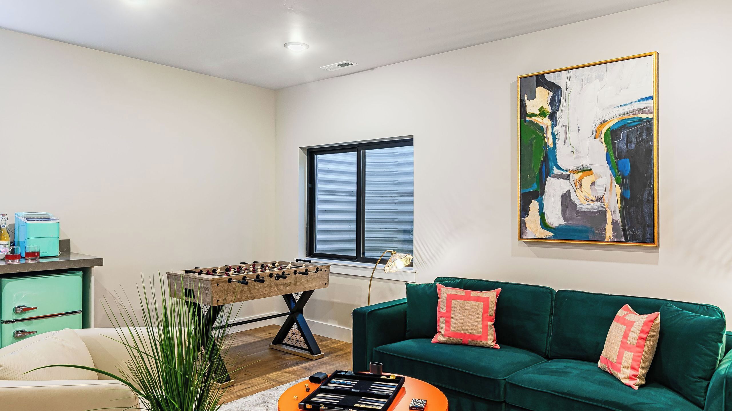 Una sala de estar con un sofá verde, una mesa de fútbol de mesa, una cafetera y un cuadro en la pared.
