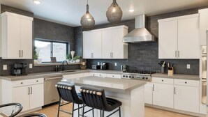 Una cucina moderna con una grande isola, mobili bianchi, una cappa in acciaio inossidabile e illuminazione a sospensione.