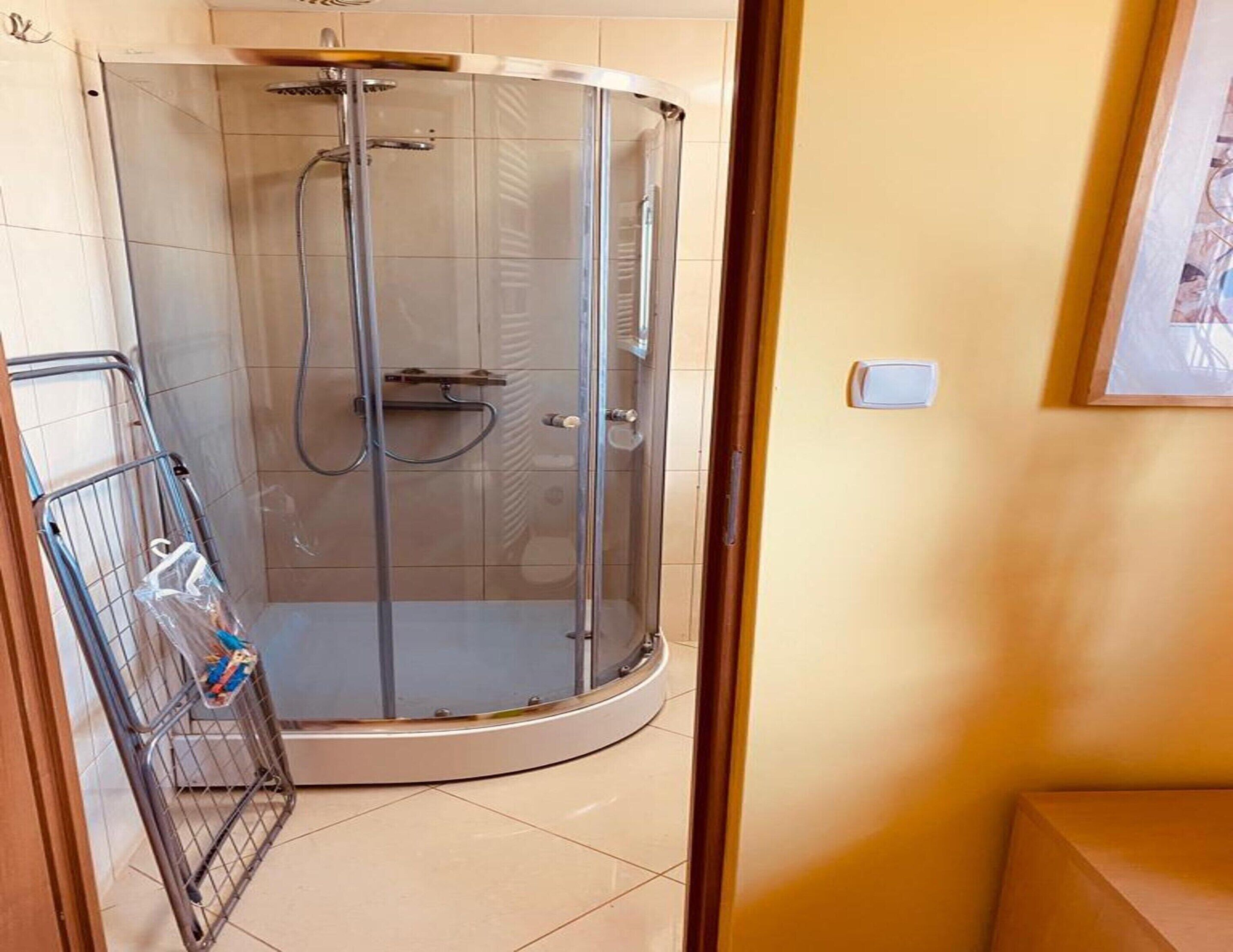 A glass-enclosed shower stall with a metal rack holding toiletries.