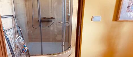 A glass-enclosed shower stall with a metal rack holding toiletries.