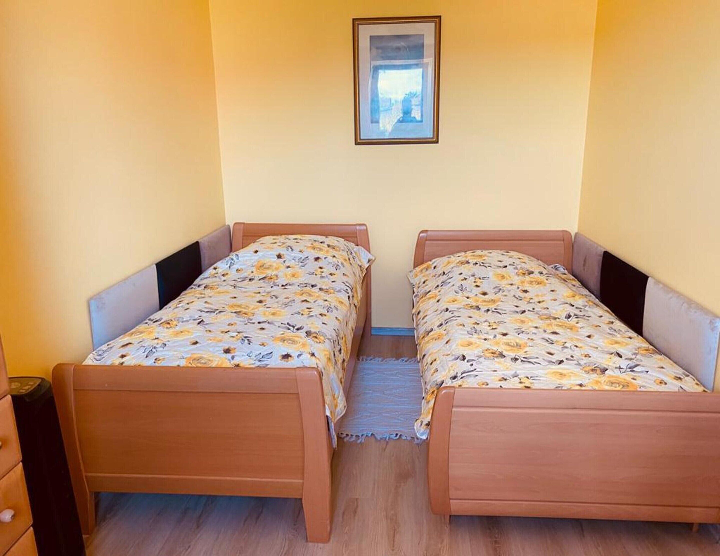 Une chambre avec deux lits en bois, dotés de draps à motifs floraux, une petite table de chevet et un tableau encadré au mur.
