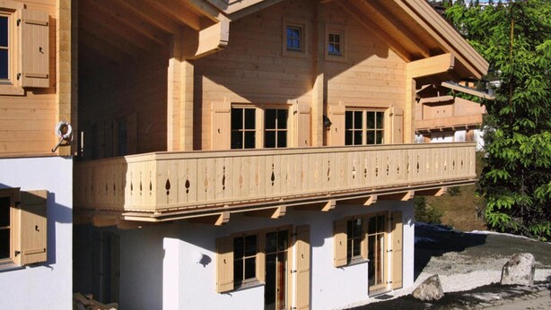 Una chalet in legno a due piani con un balcone, ampie finestre e facciata bianca.