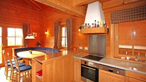 Interno di una baita in legno con angolo cottura, sala da pranzo e un'ampia finestra.