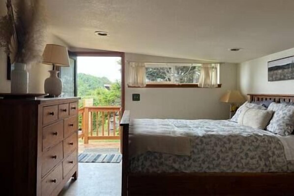 Une chambre à coucher avec un lit, une commode, une fenêtre avec des rideaux et une vue sur la verdure.