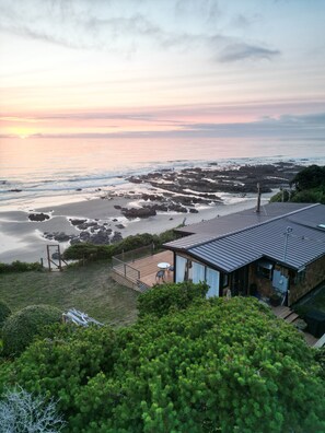 Une propriété située sur la côte, dotée d’une terrasse avec vue sur la plage, d’un petit jardin et d’un bâtiment dont le toit est en pente.