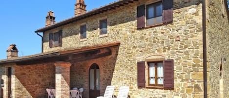 Un edificio de piedra con patio, mobiliario exterior y cielo despejado.