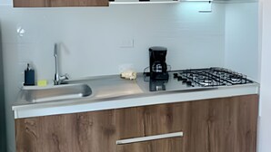 Una cocina con armarios de madera, un lavamanos de acero inoxidable, una estufa a gas y una cafetera.