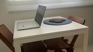 Una mesa blanca con una computadora portátil y un objeto decorativo, rodeada de sillas de madera.