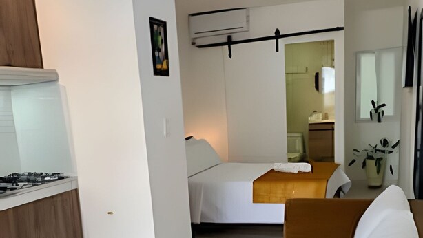 Una sala de estar moderna con un sofá marrón, una cama y una zona de cocina con estufa.