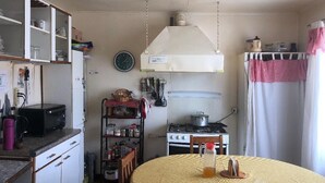 A compact kitchen with a stove, microwave, and cabinets. There is a round table with a bottle on it. - Hostal Bellavista Patagonia (Natales)