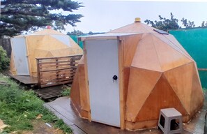 Deux structures métalliques hexagonales, dotées d’une porte et d’un petit tabouret, qui semblent servir de pièces de rangement ou de locaux techniques.