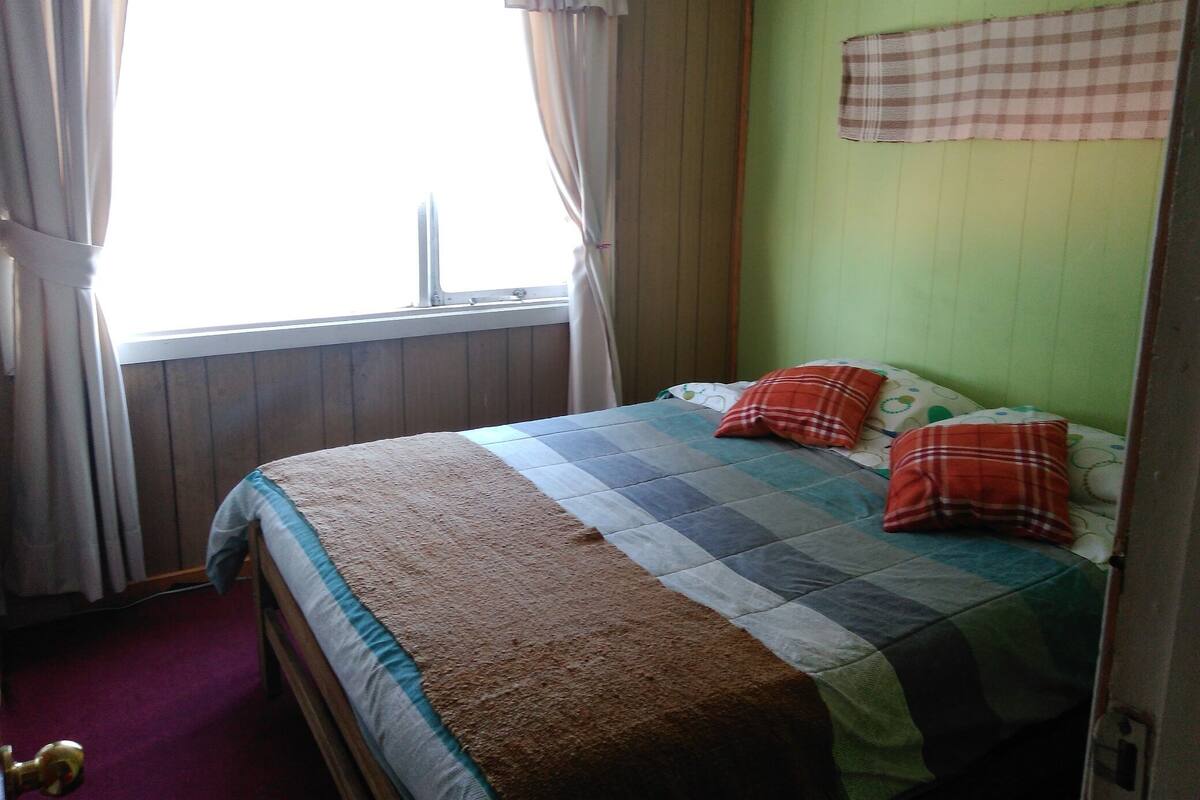 A bedroom with a bed, curtains, a window, and a green wall.