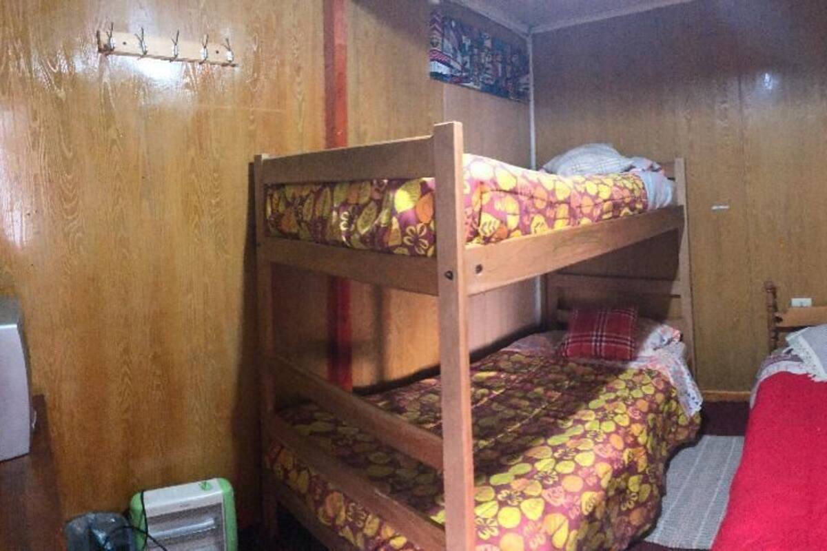 A bunk bed room with a red blanket, wooden walls, and a window with curtains.