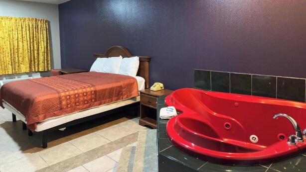 Une chambre d’hôtel avec un lit, une baignoire rouge, un ventilateur de plafond et une table de chevet avec un téléphone.