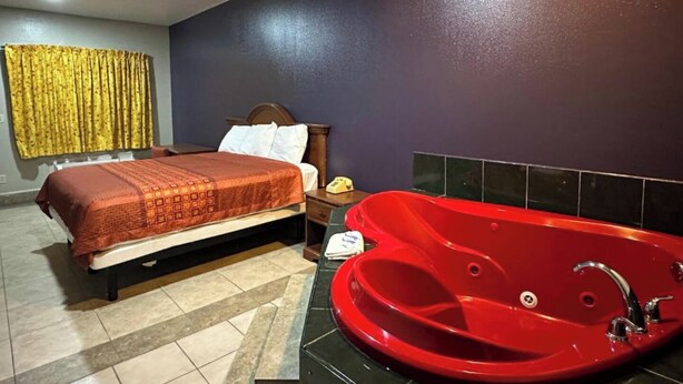 A bedroom with a bed, a red bathtub, a ceiling fan, and a curtain.