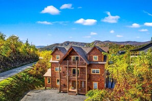 A log cabin with a front porch, a garage, and a mountain backdrop. - Indoor Pool, Volleyball Beach, Mountain View (Gatlinburg)