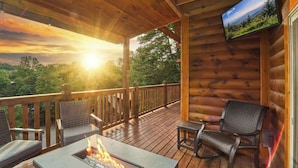 Eine Holzterrasse mit Feuerstelle, Sitzgelegenheiten im Freien und einem an der Wand montierten Fernseher.