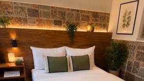 Un lit bien fait, avec une tête de lit en bois, une table de chevet avec une lampe, et un mur en pierre derrière le lit.