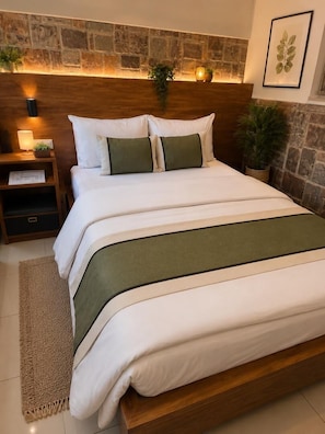 A neatly made bed with a wooden headboard, a bedside table with a lamp, and a stone wall behind the bed. - Africa Luxury Tours & Accommodation (Kigali)