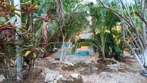 A tropical garden with a small pool surrounded by lush vegetation and rocks. - La casa de piedra y colores  (Tinum)