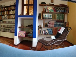 Ein Zimmer mit einer Bücherwand, einem Korbsessel und einem kleinen Tisch mit einem Teekessel.