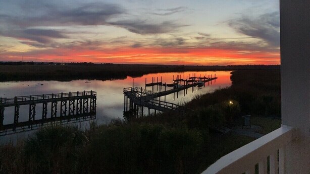 A sunset view from a balcony overlooking a calm water body with docks. - Beautiful, Newly-Renovated Condo on the Altamaha River in Darien with BoatSlip (Darien)