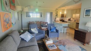 A living room with a grey sofa, two armchairs, a coffee table, and a rug. There is a kitchen in the background with a dining area. - Beautiful, Newly-Renovated Condo on the Altamaha River in Darien with BoatSlip (Darien)