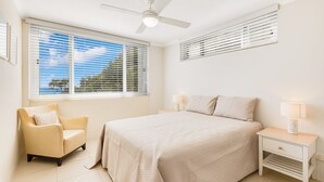 Un dormitorio con cama, una silla, una mesita de noche, ventilador de techo y ventana con persianas.