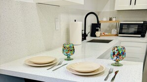 Una cucina con un piano di lavoro bianco, due sgabelli da bar blu, un forno a microonde e un lavandino.
