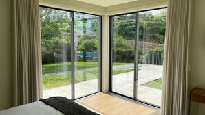 Un dormitorio con un amplio ventanal corredera que da a un balcón con vistas a zonas verdes y un edificio al fondo.