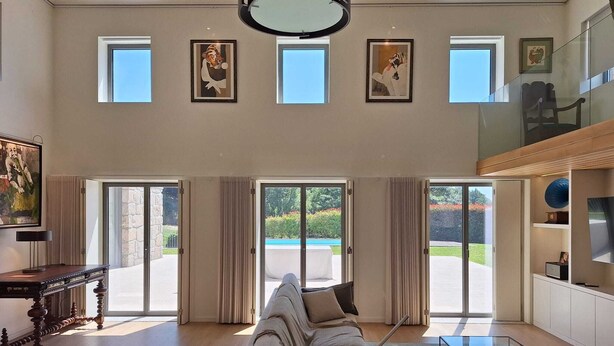 Amplia sala de estar con un sofá grande, una mesa de centro de vidrio y una chimenea. Varias ventanas ofrecen luz natural y vistas al exterior.