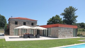 Un edificio de piedra con techo rojo, piscina y mobiliario de exterior.