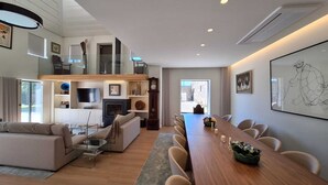 Una sala de estar moderna con sofá, televisión, chimenea y un comedor con una mesa larga y sillas.