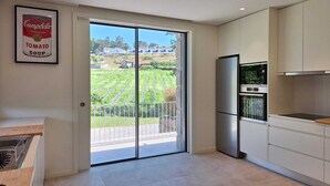 Una cocina moderna con un amplio ventanal corredera que da a un balcón con vistas a un campo verde.