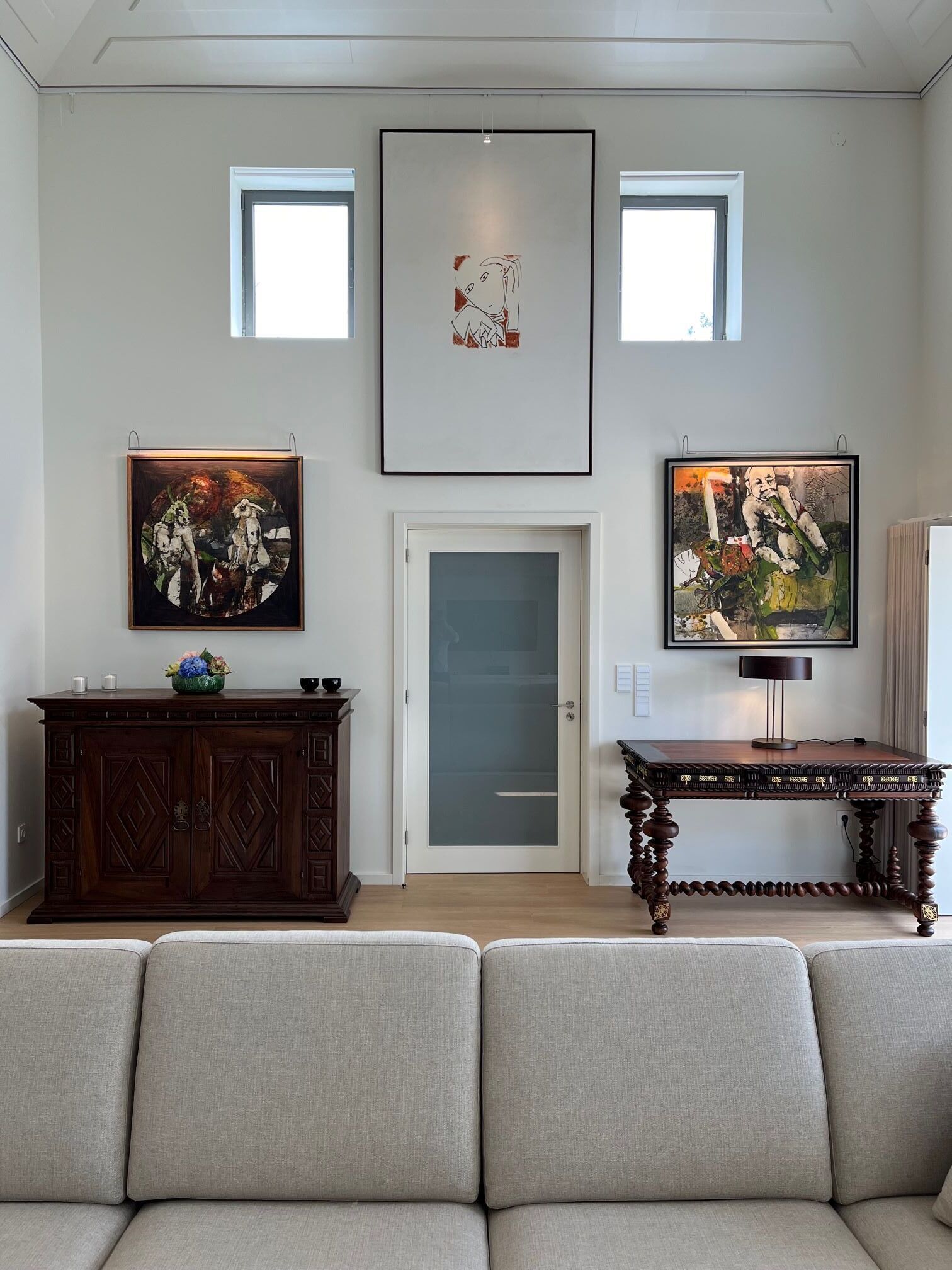 Un salon avec un canapé, un meuble et une table sur laquelle sont exposées des œuvres d’art. Il y a une porte et une fenêtre.