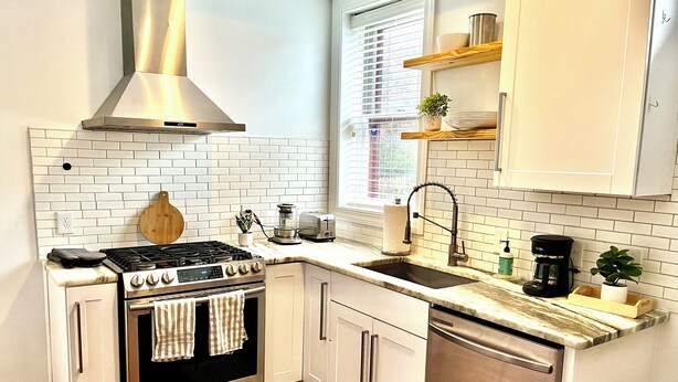 A compact kitchen with a gas stove, oven, and dishwasher, white cabinets, and a window with blinds.