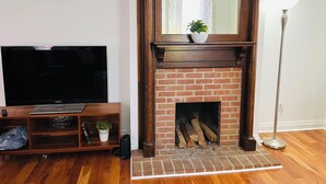A living room with a brick fireplace, a television on a wooden stand, and a floor lamp.