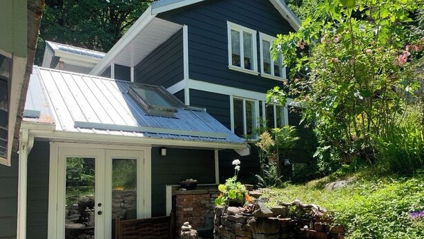 Ein Haus mit überdachter Veranda, einer Steinmauer und einem Garten mit verschiedenen Pflanzen und Blumen.
