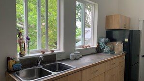 Eine Küche mit großem Fenster, einem Spülbecken, Holzschränken und einem schwarzen Kühlschrank.