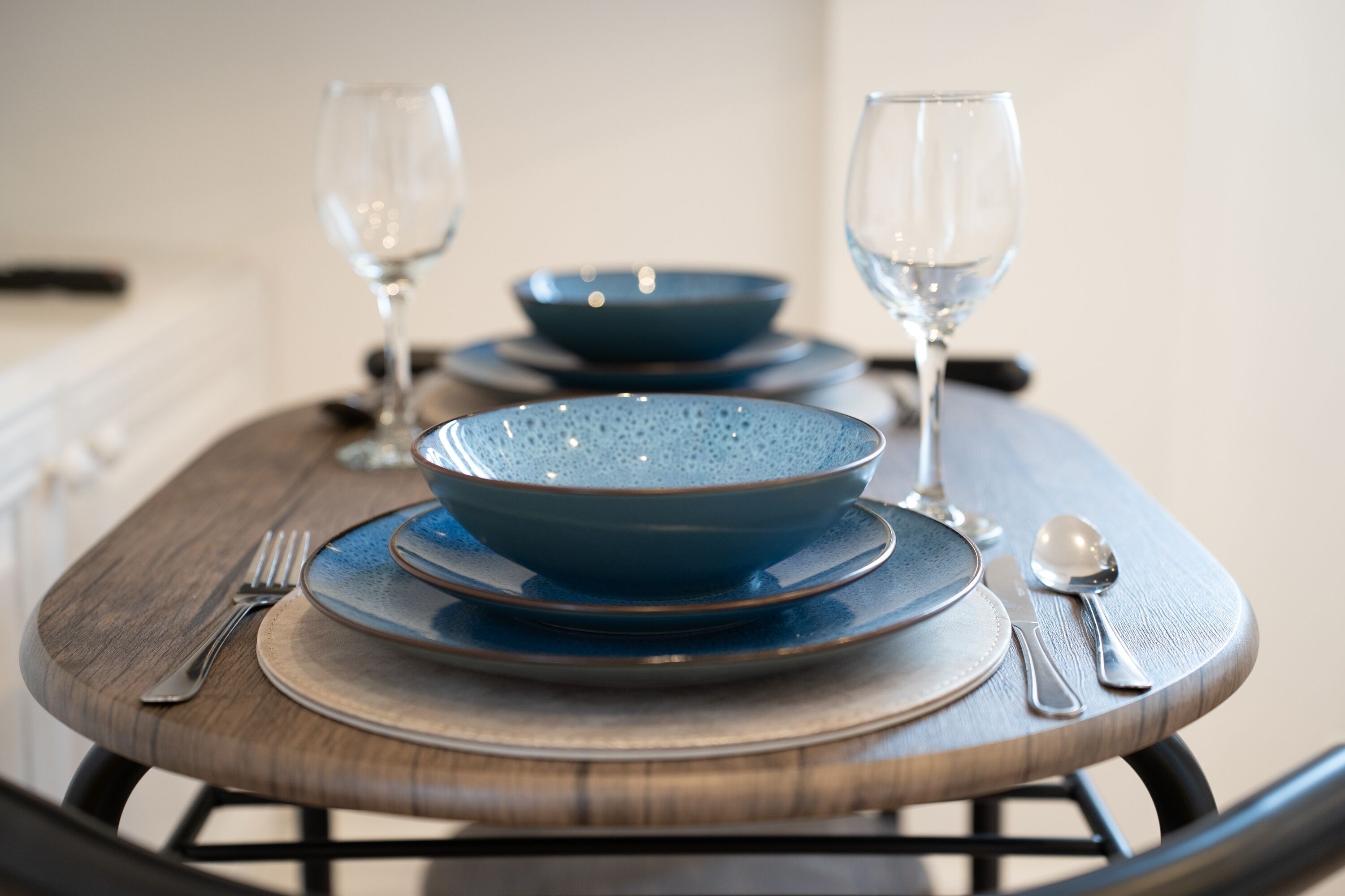 Une table à manger dressée avec de l’assiette bleue, des bols et des couverts en argent, accompagnée de deux verres à vin.