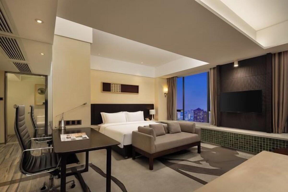 A hotel room with a bed, a sofa, a desk, and a TV.