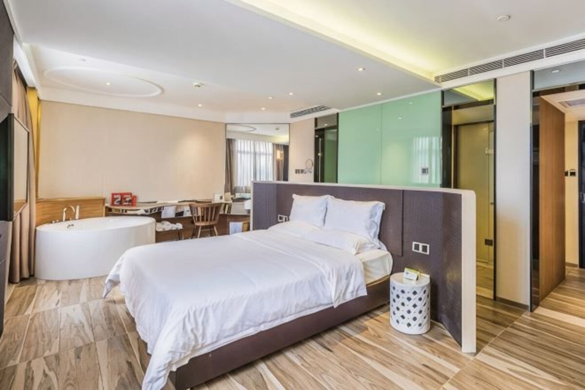 A modern hotel room with a large bed, a separate bathroom, a desk, and a view of the city.