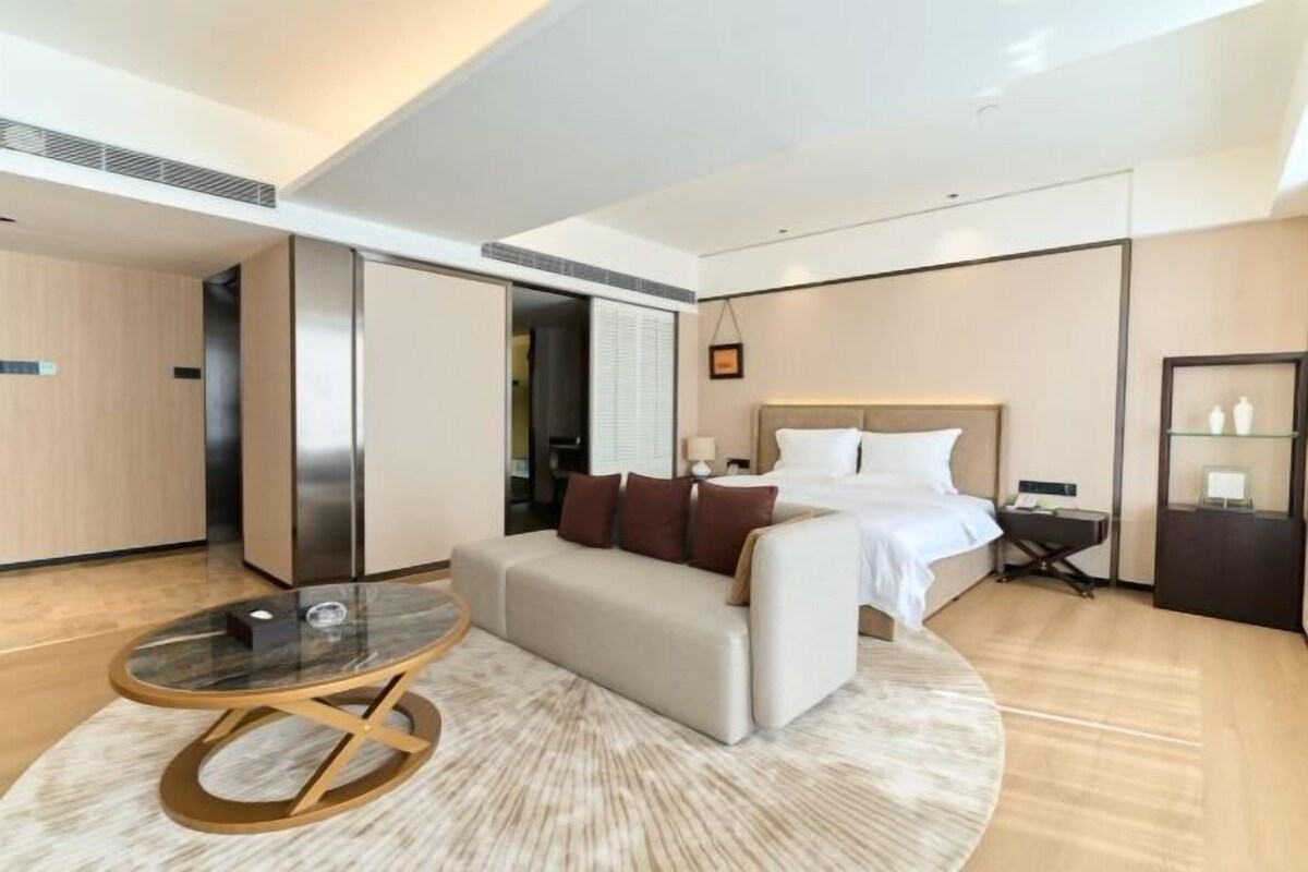 A modern hotel room with a bed, a sofa, a coffee table, and a desk.