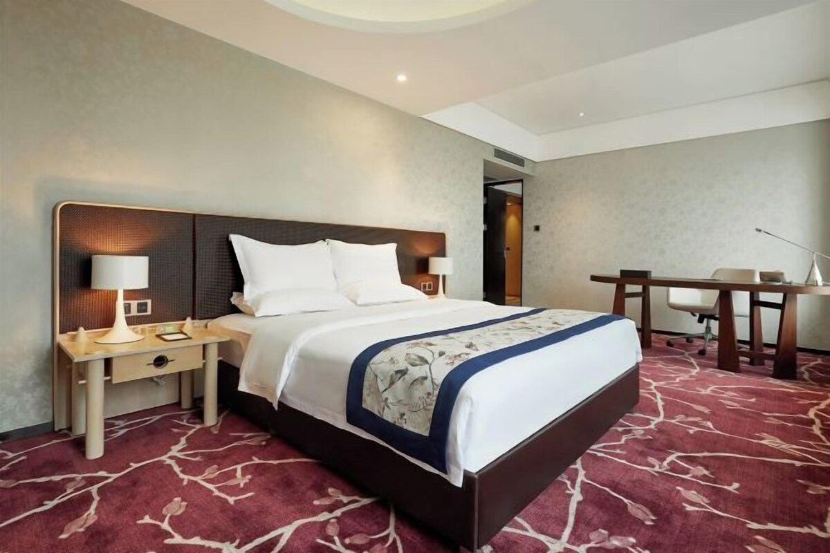 A hotel room with a large bed, bedside tables with lamps, a desk, and a chair.